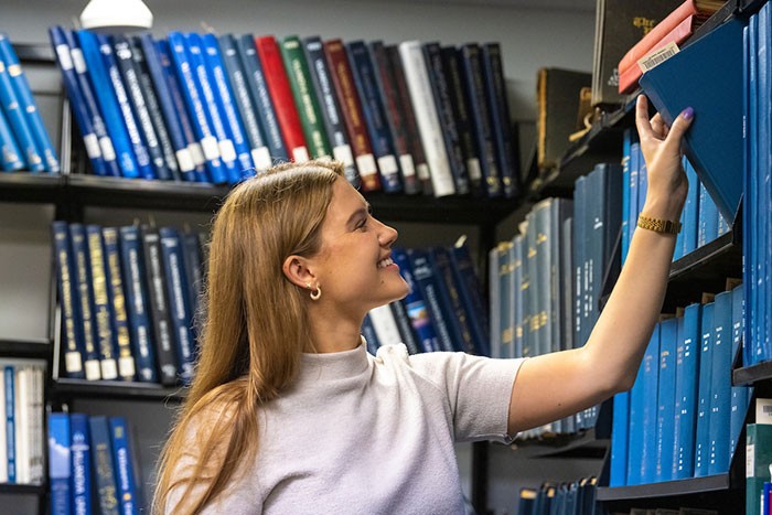 Female student pulling book from shelf