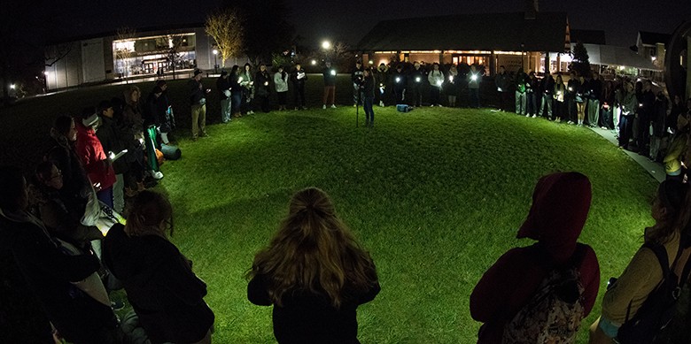 students in circle at nighttime outdoor prayer vigil holding candles