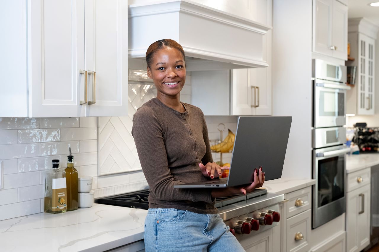 woman holding laptop looking at the camera in a kitchen