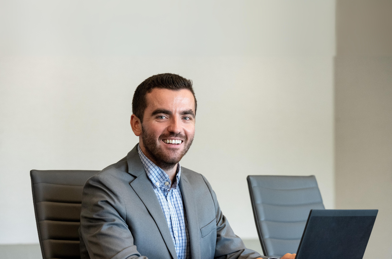 man at desk with laptop smiling at camera