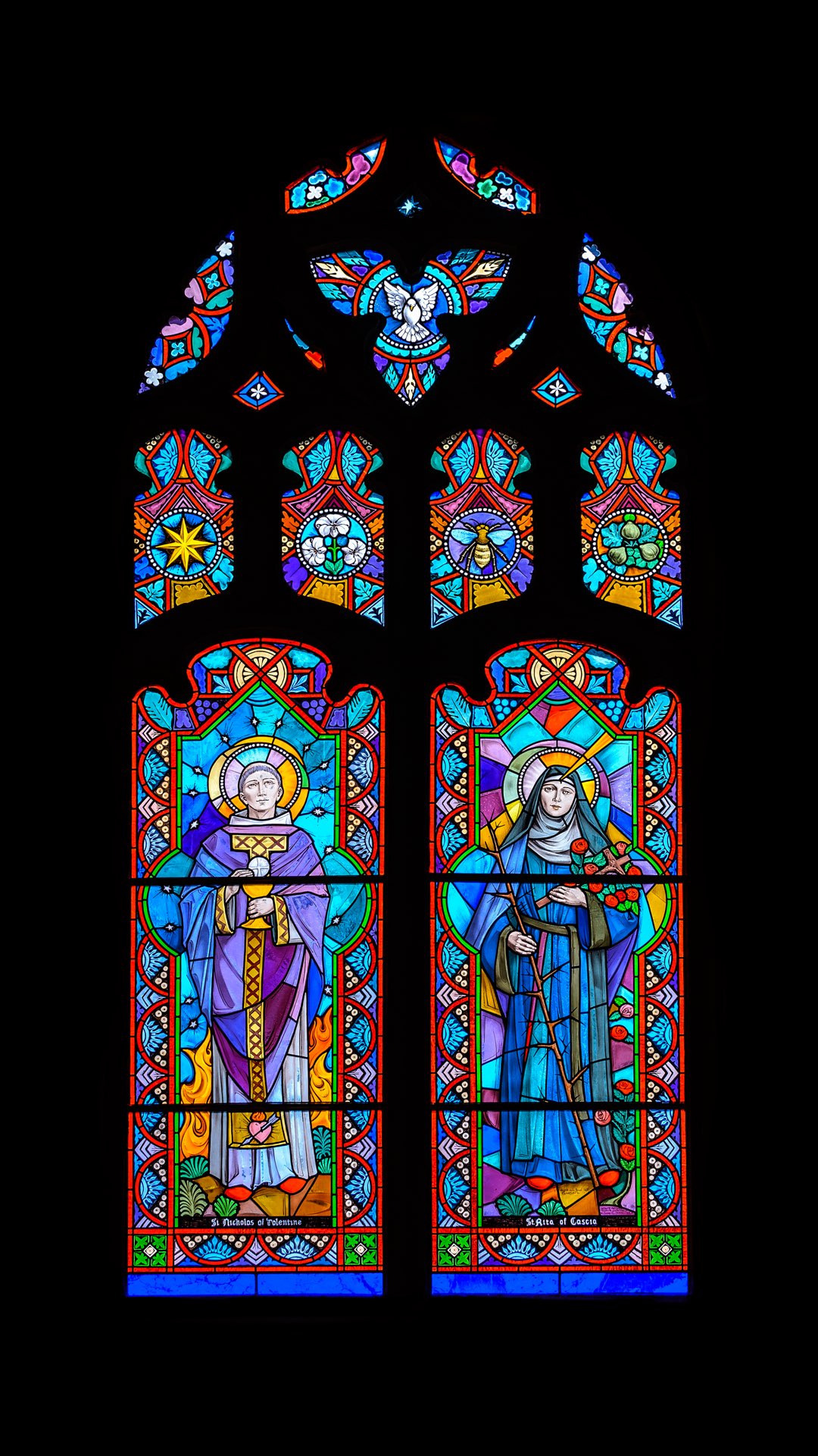 Stained glass windows depicting Saint Nicholas of Tolentine and Saint Rita of Cascia.