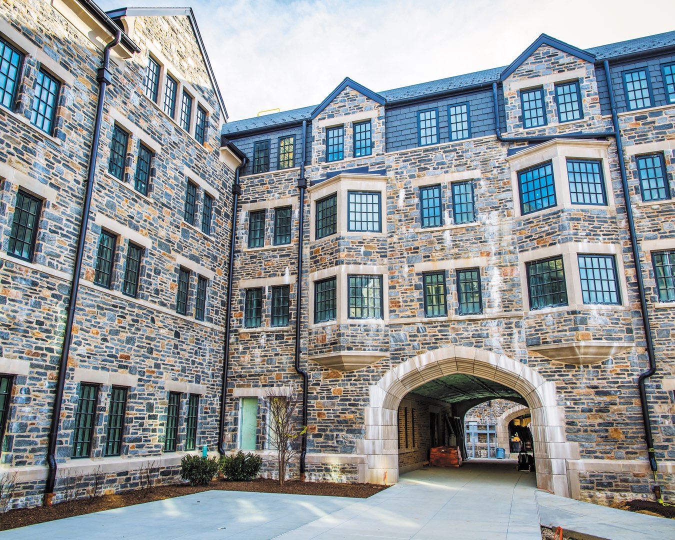 Exterior of The Commons residence halls showing black casement windows, gothic arches, stone facade and faux slate 