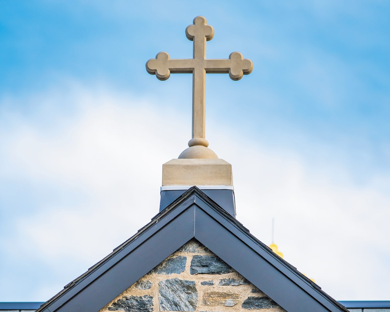 Against a bright blue sky, a cast-stone cross adorns the black roof of The Commons residence halls