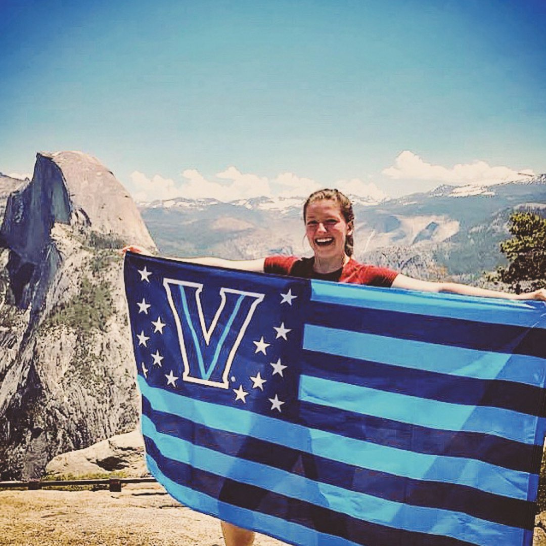 A female student holding a Villanova American flag at the top of a mountain