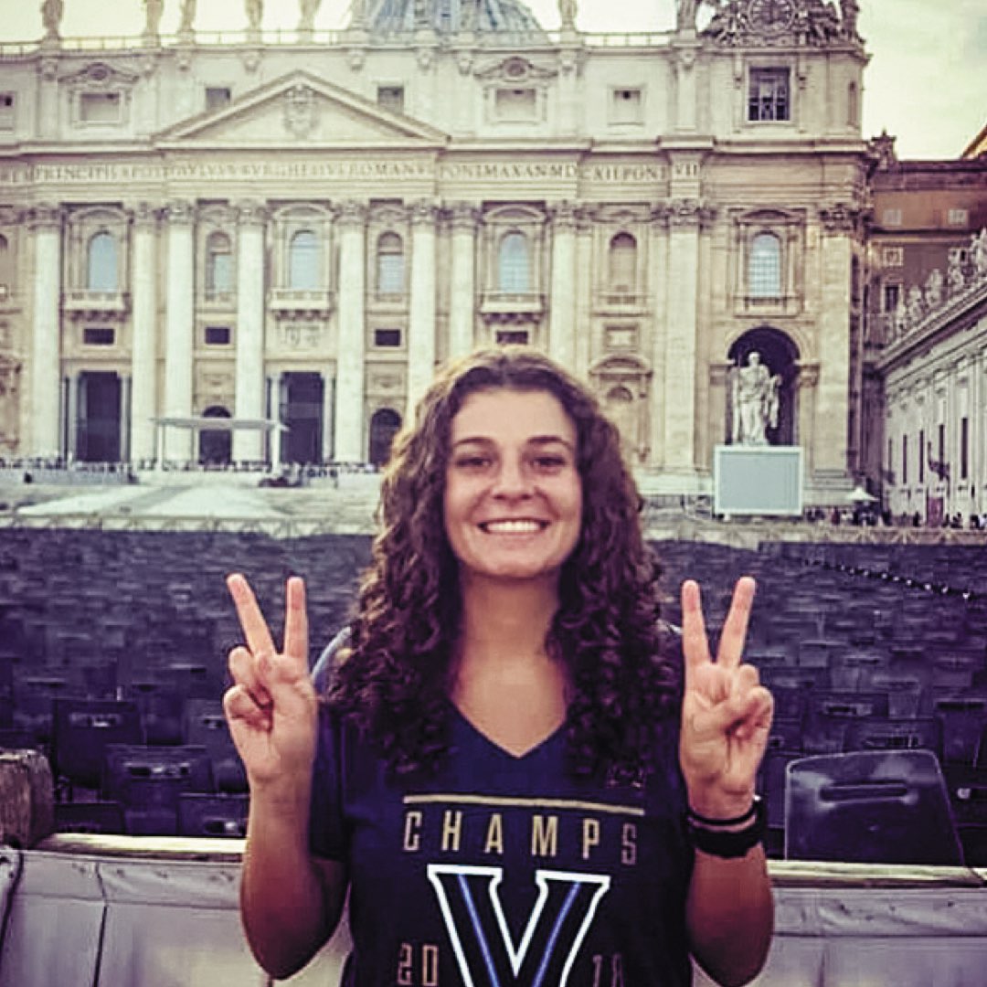 A female Villanova alumna with her Vs up wearing a 2018 NCAA Champs shirt in front of St. Peter’s Basilica in Rome 