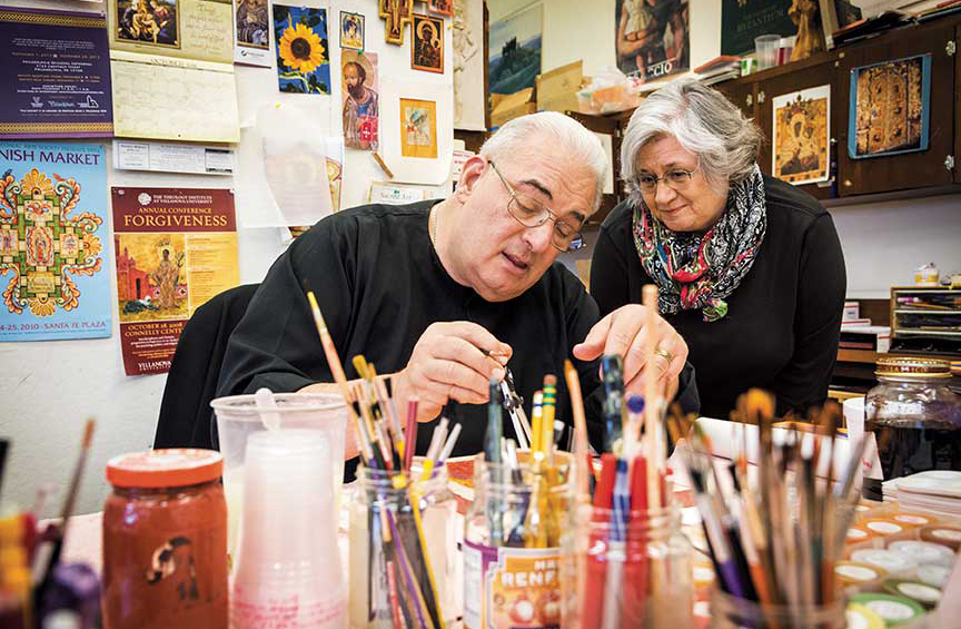 Father Richard Cannuli, seated, teaches a standing female student an art technique