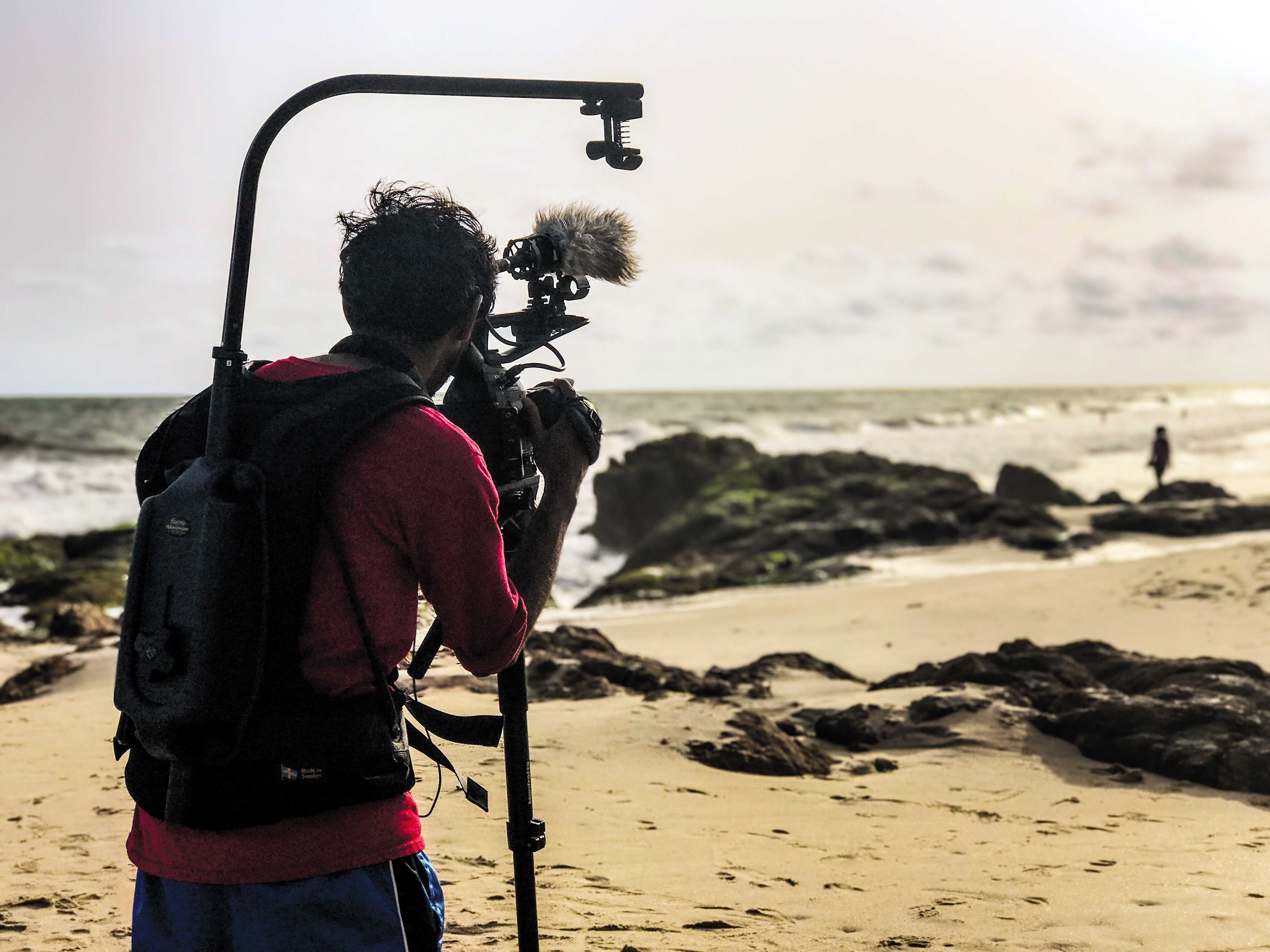 Student filming with camera on beach in Ghana