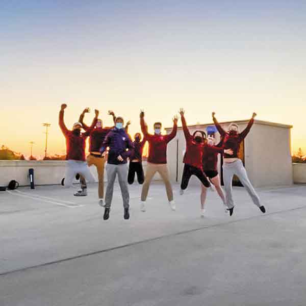 group of Villanova students wearing face masks and jumping for joy on a rooftop