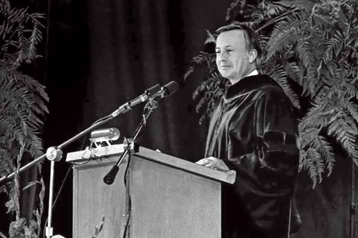 black and white photo of J. Willard O'Brien in academic dress speaking at a podium