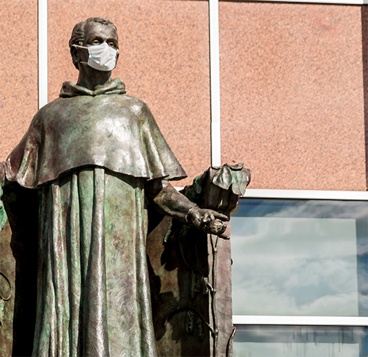 a bronze statue of Gregor Mendel wearing a white face mask