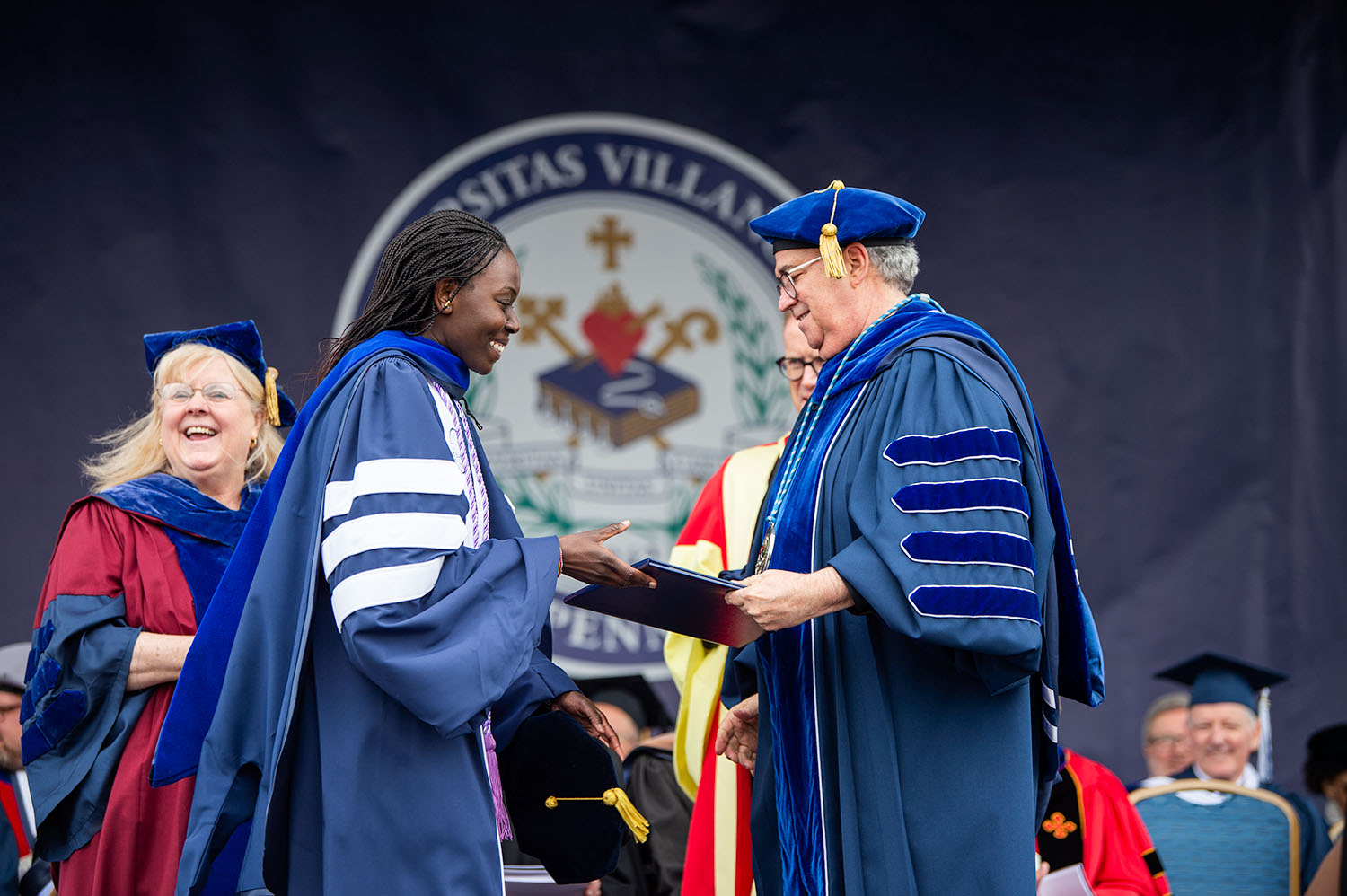 Female Villanova student wearing a graduation robe and receiving her diploma.