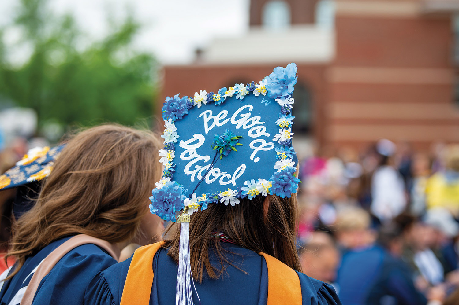 Female Villanova student wearing a graduation robe and mortarboard decorated with flowers and slogan “Be Good. Do Good.”