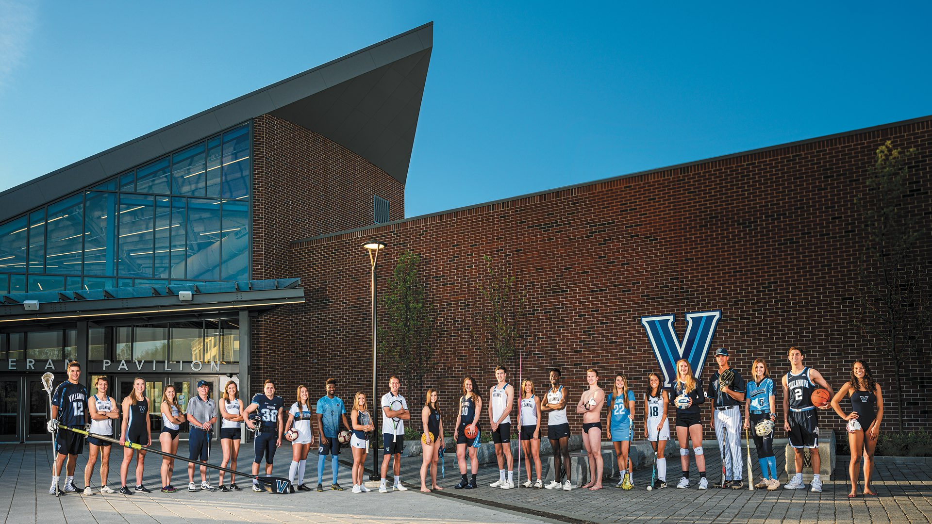 Lined up in front of Finneran Pavilion, 24 Villanova student-athletes in uniform representing various sports