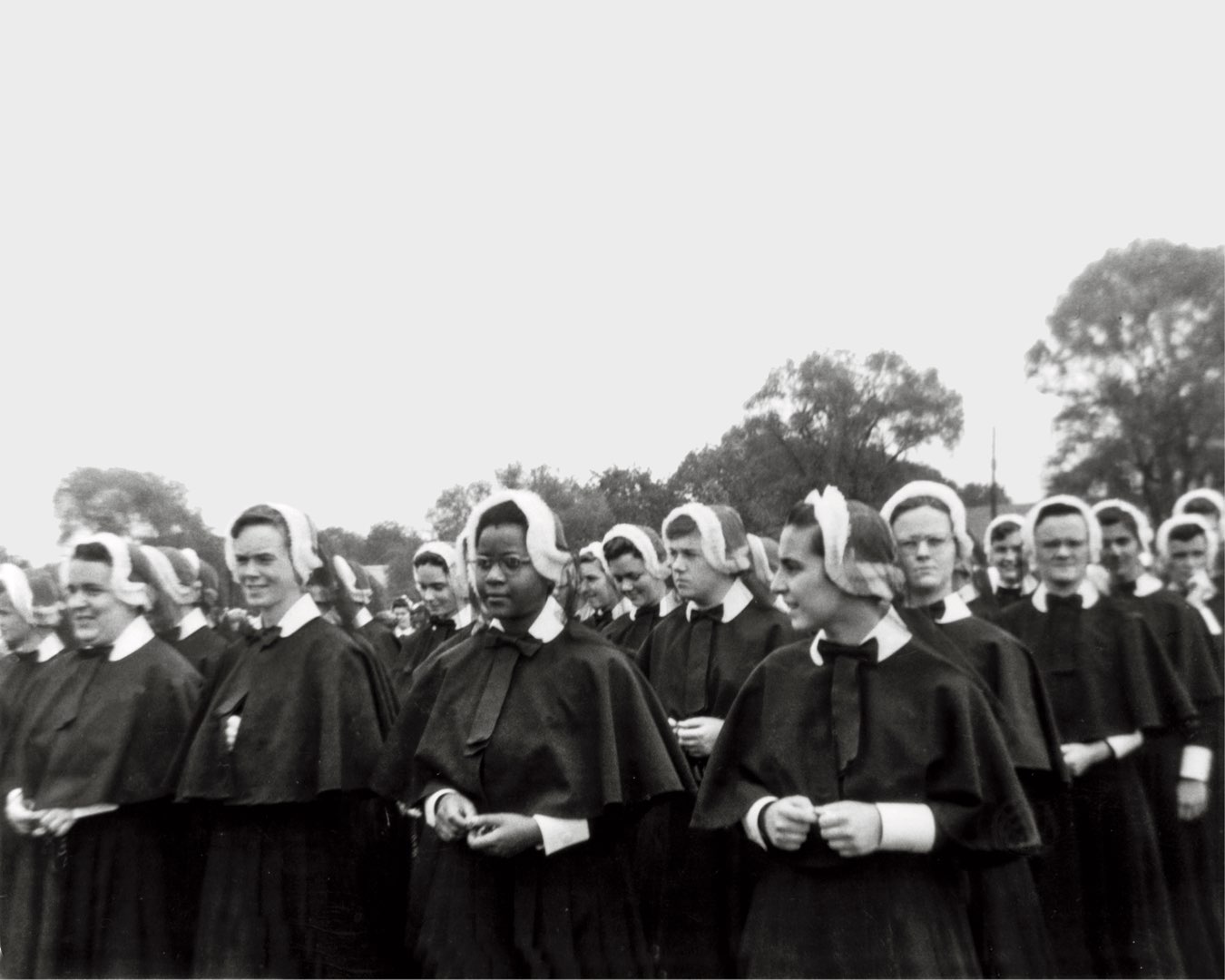 A black-and-white photo of a young Sister Cora Billings in habit amid a large crowd of novitiate nuns