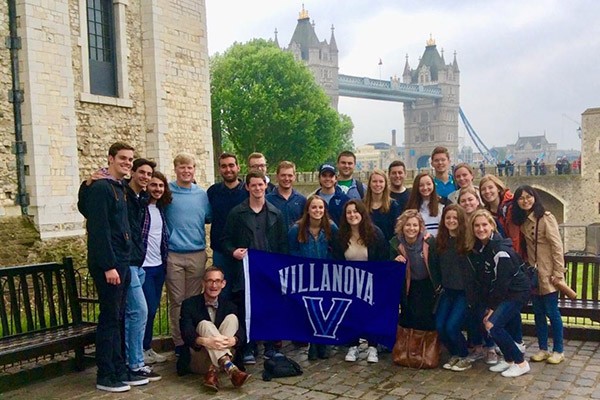 A group of students pose together with a Villanova banner with London Bridge in the background.