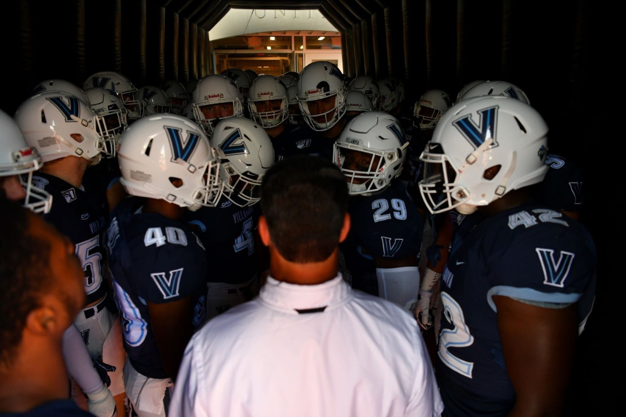 Football players standing around head coach Mark Ferrante in a tunnel