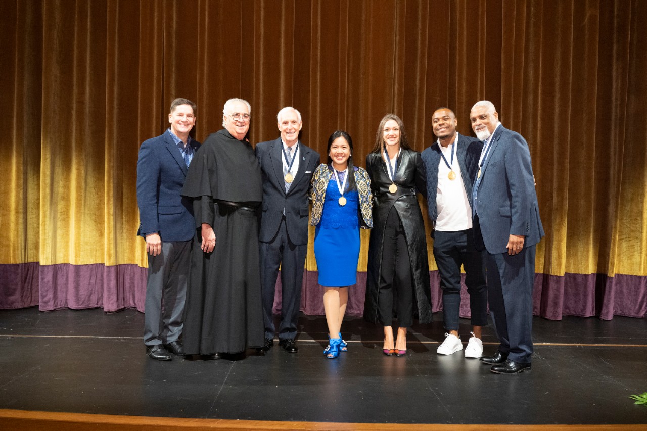 George Kolb '84, AVP of Alumni Relations, and the Rev. Peter M. Donohue, OSA, posing on stage with five alumni award winners
