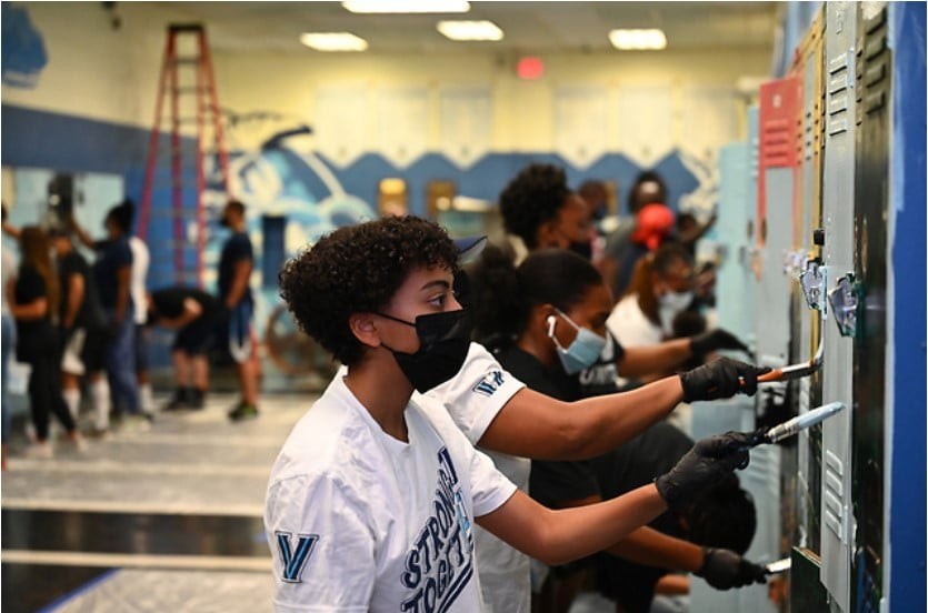 Alumni and students painting lockers in a school