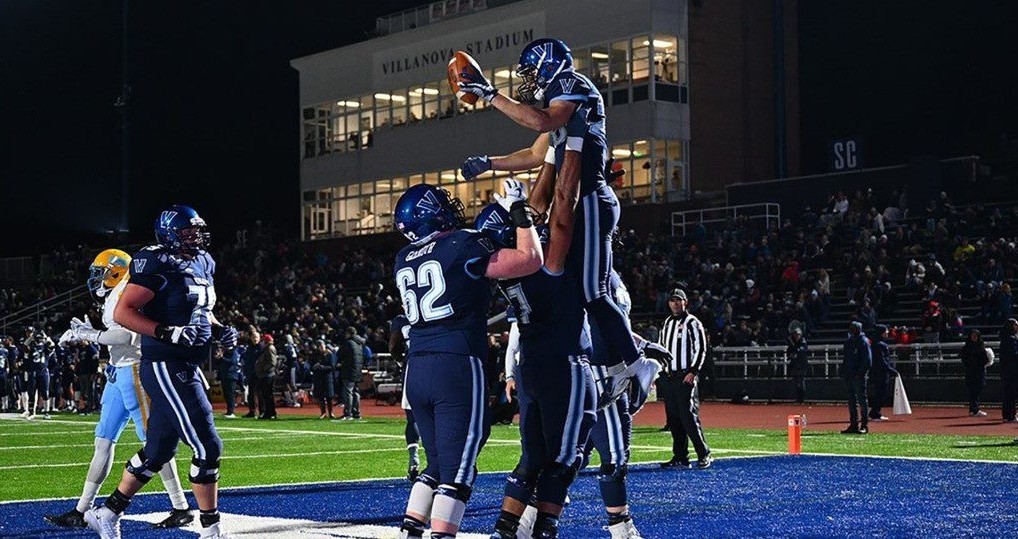Two Villanova Football players holding up a team mate with the football in the end zone at Villanova Stadium