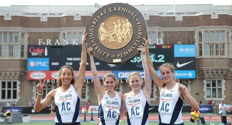 Four female track and field athlets holding up Penn Relay medal
