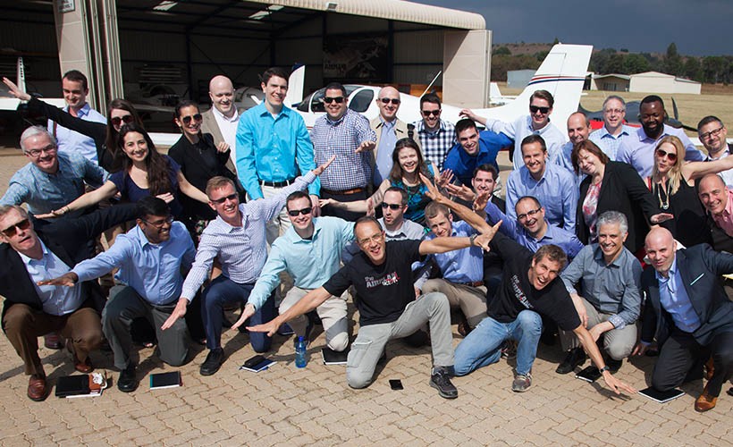EMBA students on an international immersion pose in front of a small plane at an airport.