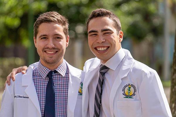 Two students wearing medical lab coats for the University of Puerto Rico pose together.