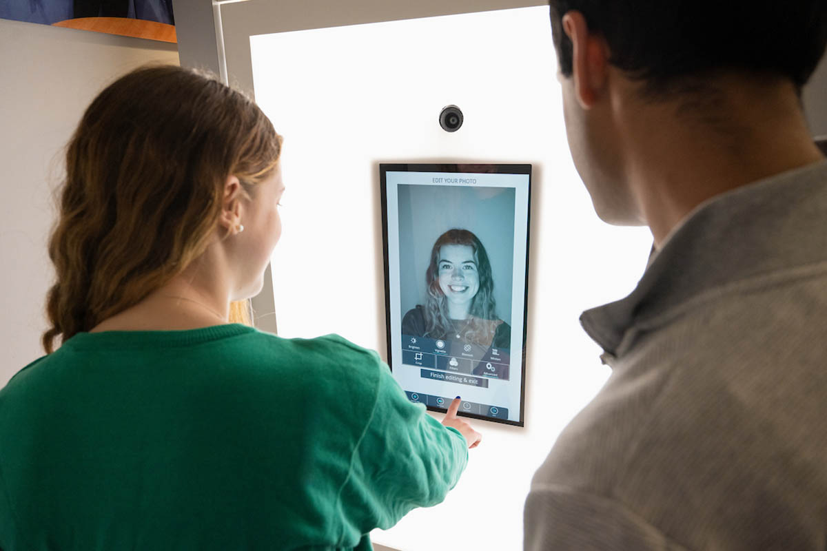 Two students looking at a screen with an image of one of the student's headshots displayed on it.
