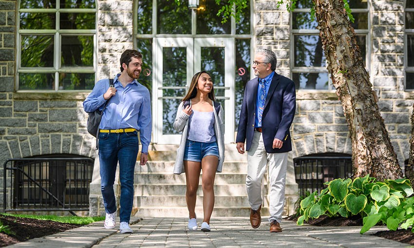 Faculty member walking with two Villanova students outside Tolentine Hall.