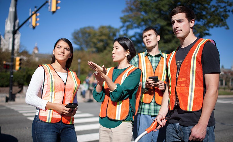 Associate Professor Seri Park, who focuses on transportation engineering, stands with three students in orange vests observing a main intersection on Villanova's campus.