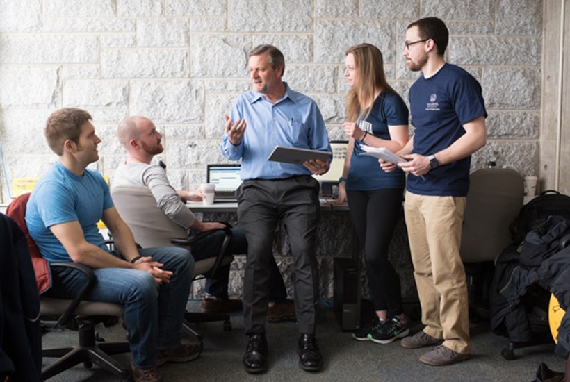 A professors talks with students in a classroom.