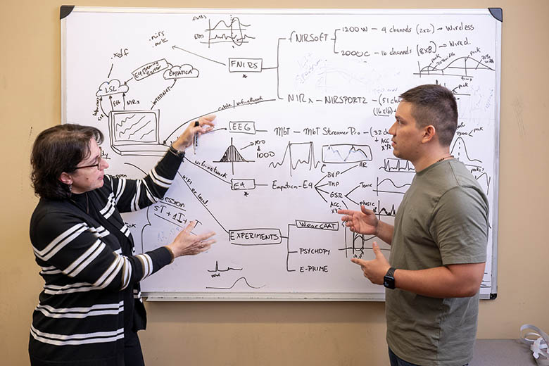 A student and professor looking at a whiteboard with fNIRS calculations