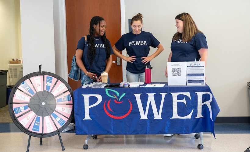 Three students staff a POWER table at a campus event