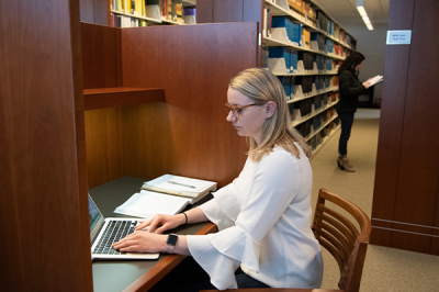 female student doing research on laptop in a library