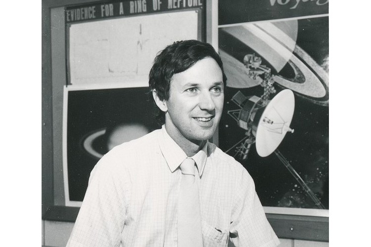 Dr. Guinan sits in front of his research team's poster displaying evidence for a ring around Neptune in 1982.