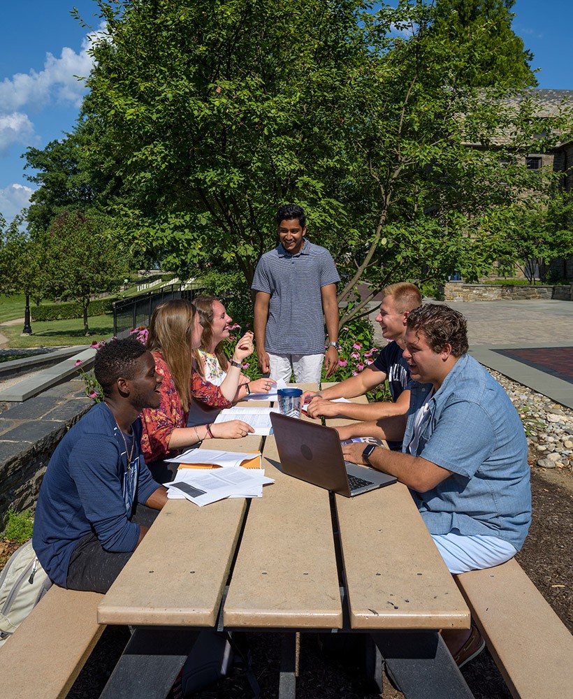 A group of students work together at a table outside.