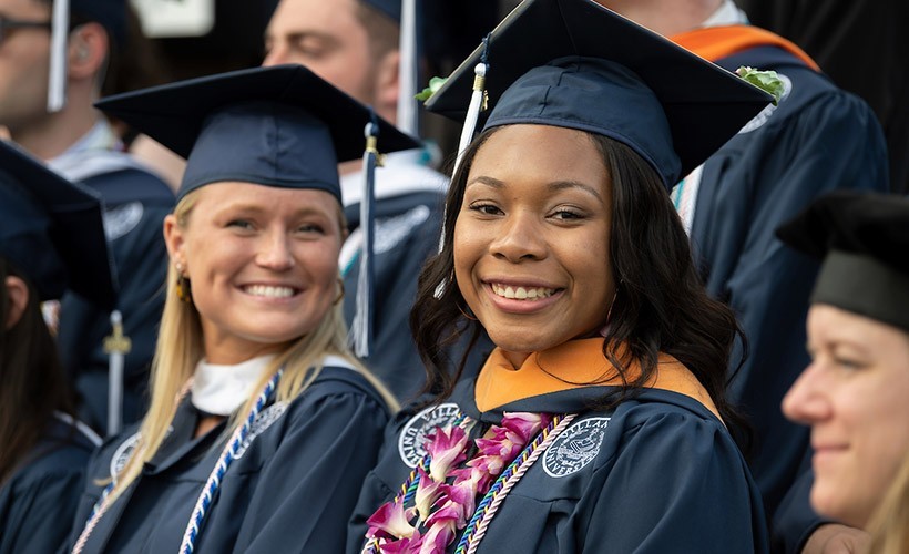 Two graduates smile at commencement.