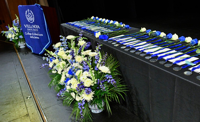 A table with medallion awards on a stage with blue and white flowers.