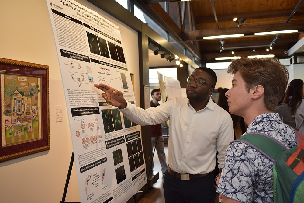 Graduate student explains research displayed on a poster