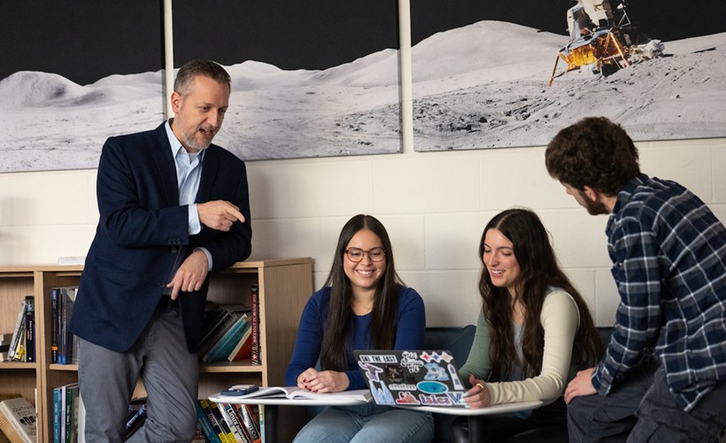 Faculty member and three students talk in lounge. 