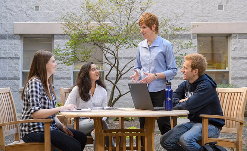 Students interact with a professor around a table.