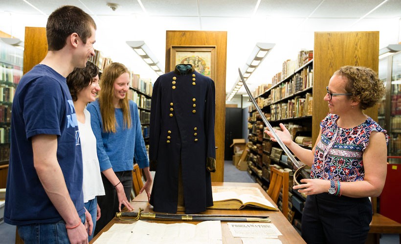 Students and a faculty member observing artifacts in a library.