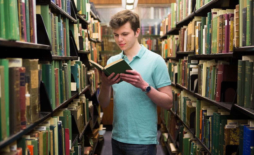 Student in library stacks reading a book.