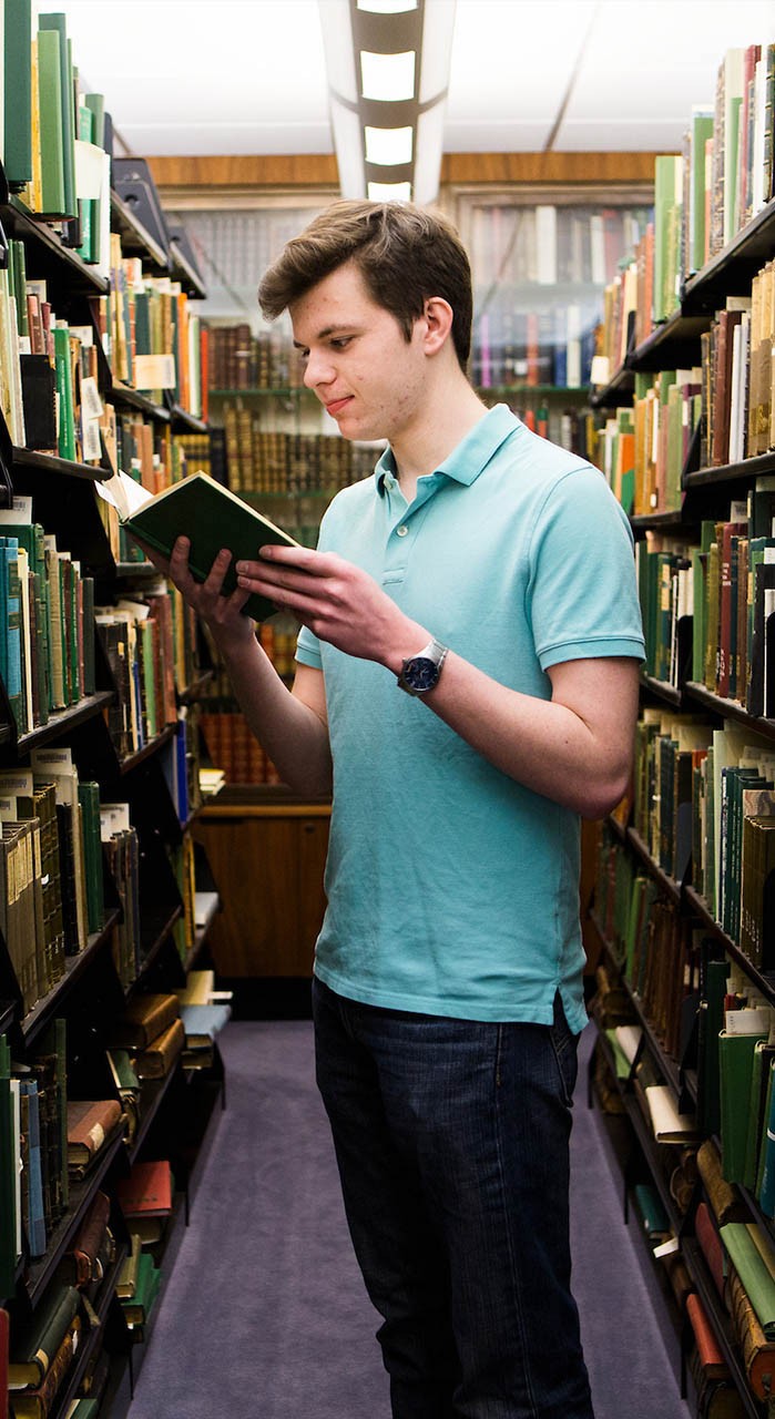Student reads a book in the library stacks.