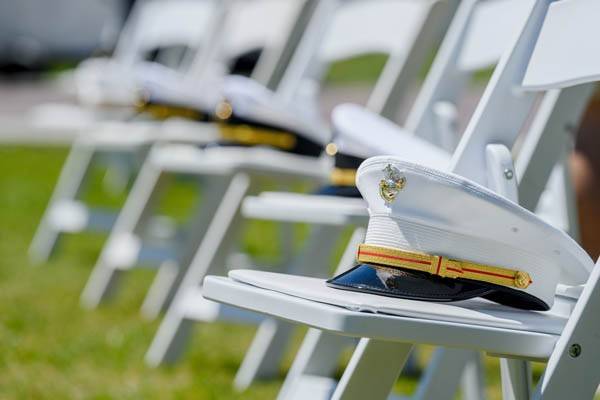 white folding chairs on grassy field with white military hats on seats