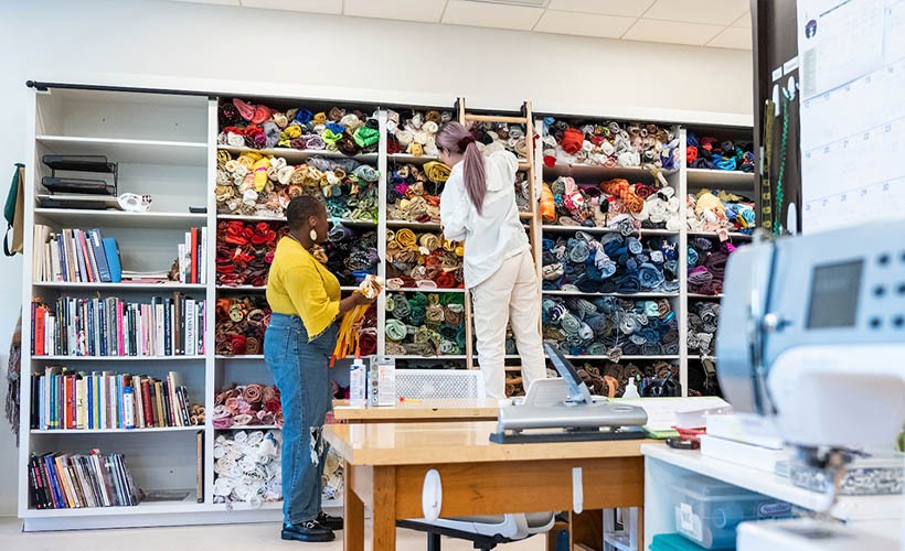 Two graduate students sorting colorful fabrics in the costume shop