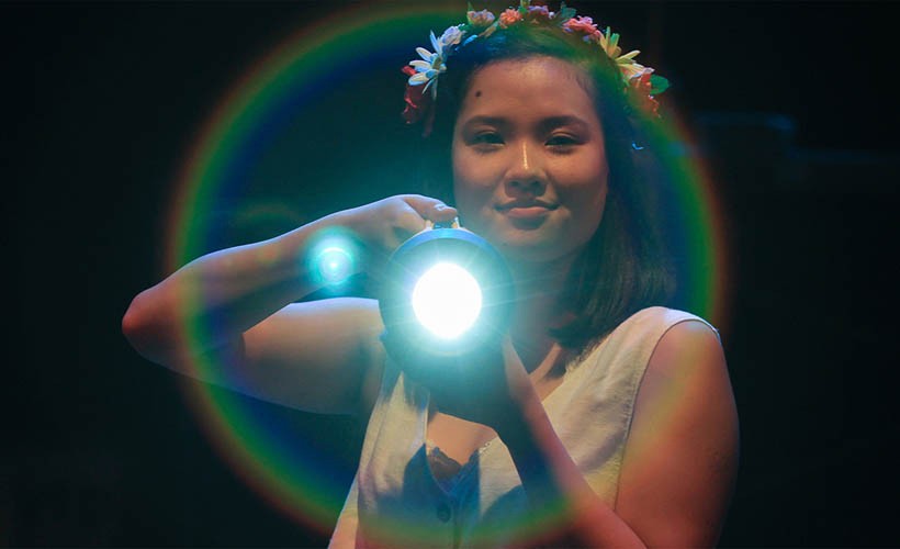 Actor from the musical Godspell shining a flashlight at the viewer