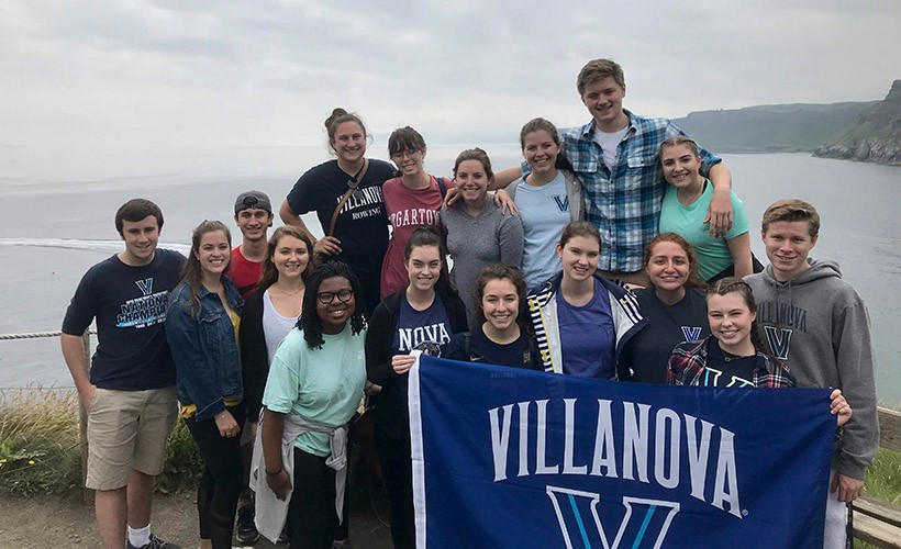 A group of students stand on the cliffs of Ireland with a Villanova flag.