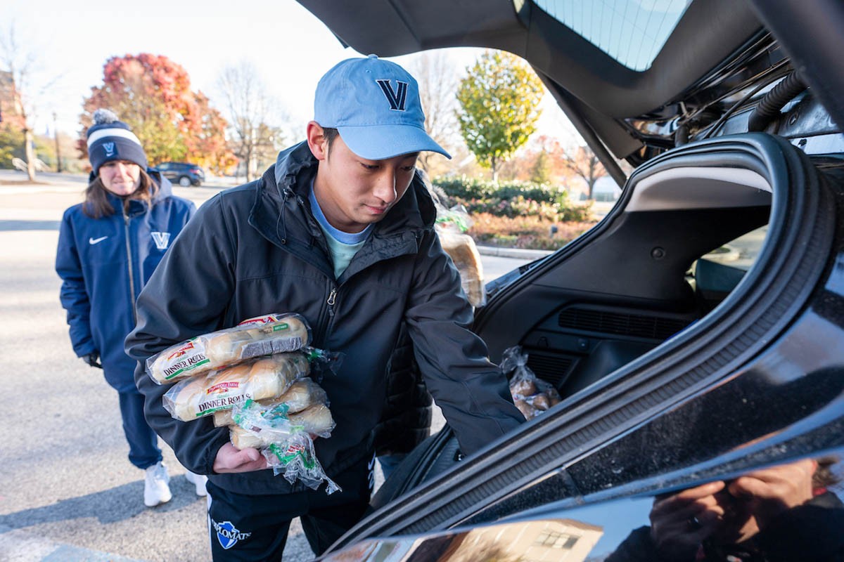 Male student in a Villanova hat putting bread into a car trunk