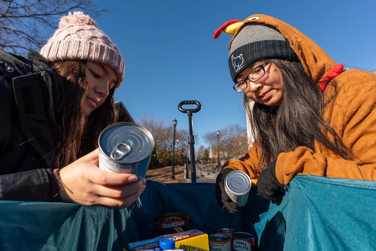 Two students placing cans in a bag