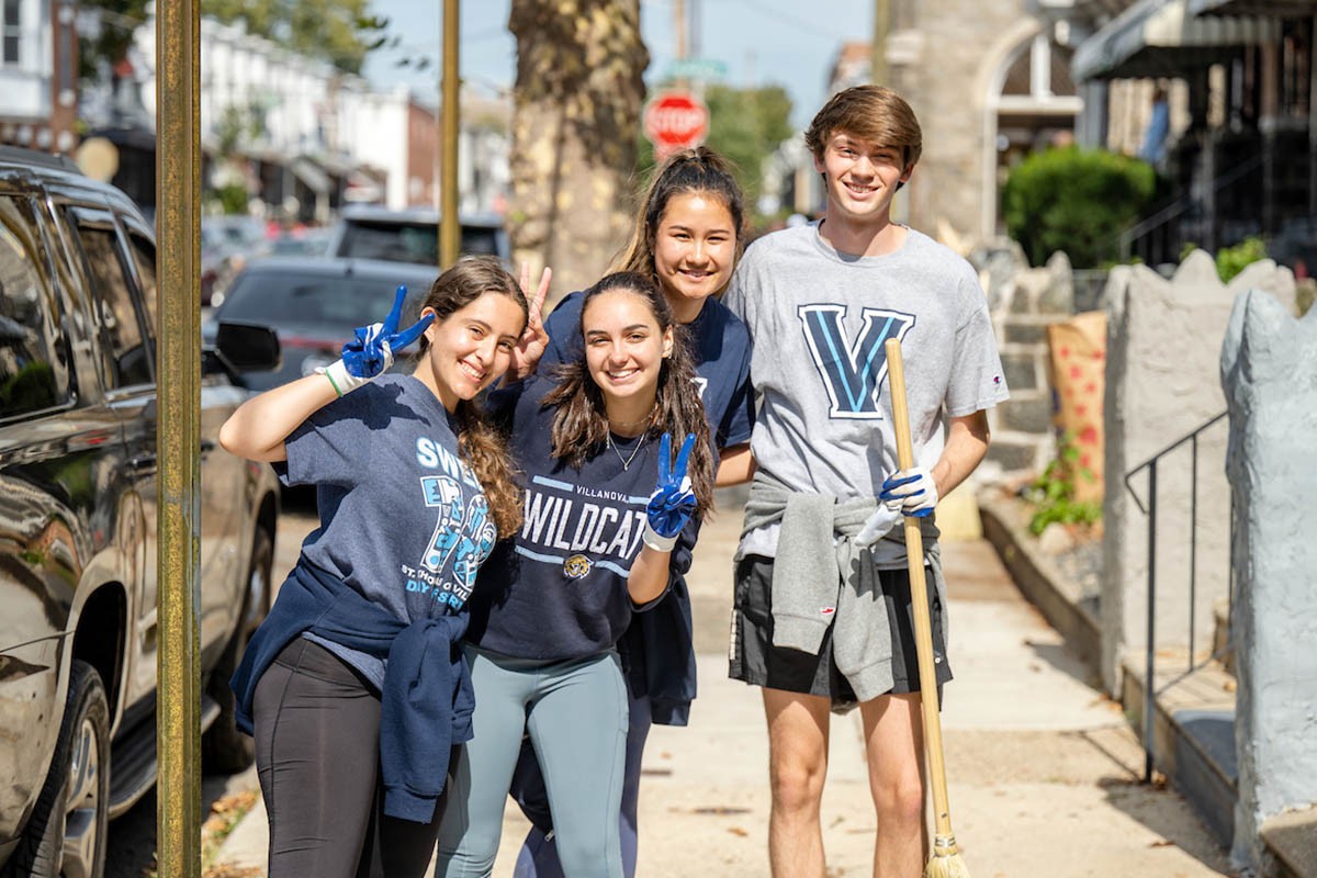 Four students doing service and throwing up the Villanova "V"